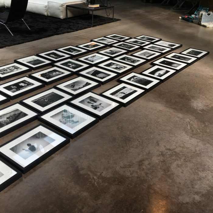 Many b/w pictures on the floor getting ready to be installed on a wall