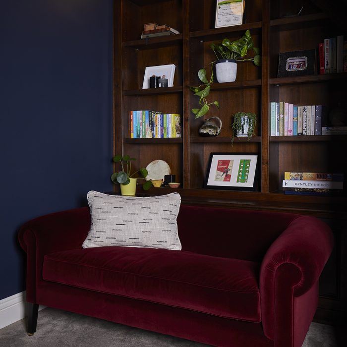 A burgundy velvet sofa and dark blue wall